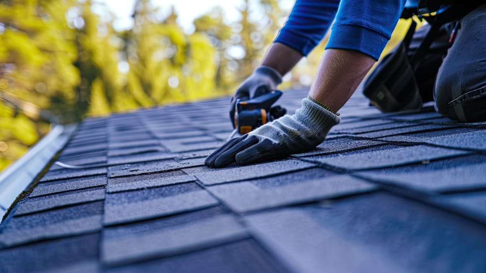 A roofing contractor performing professional shingle roof installation and weatherproofing near the eavestrough edge.